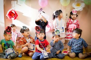 Young children in festive costume holding craft items in a decorated classroom