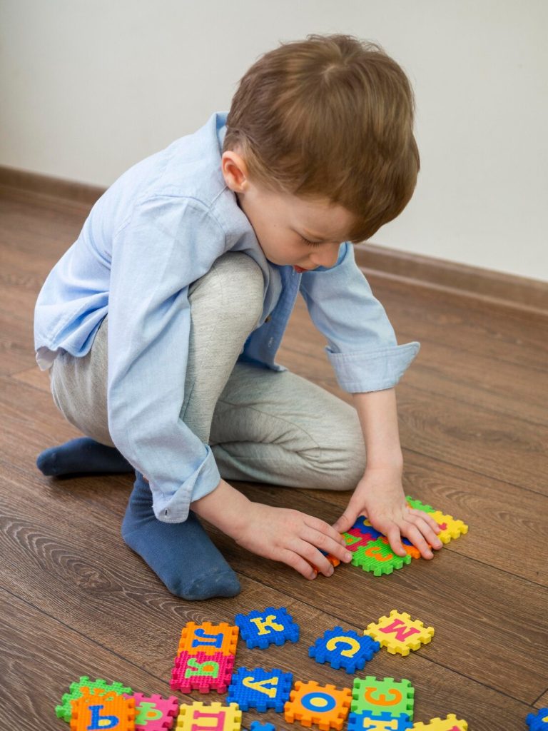 A boy kneeling on the floor putting together alphabet puzzle tiles